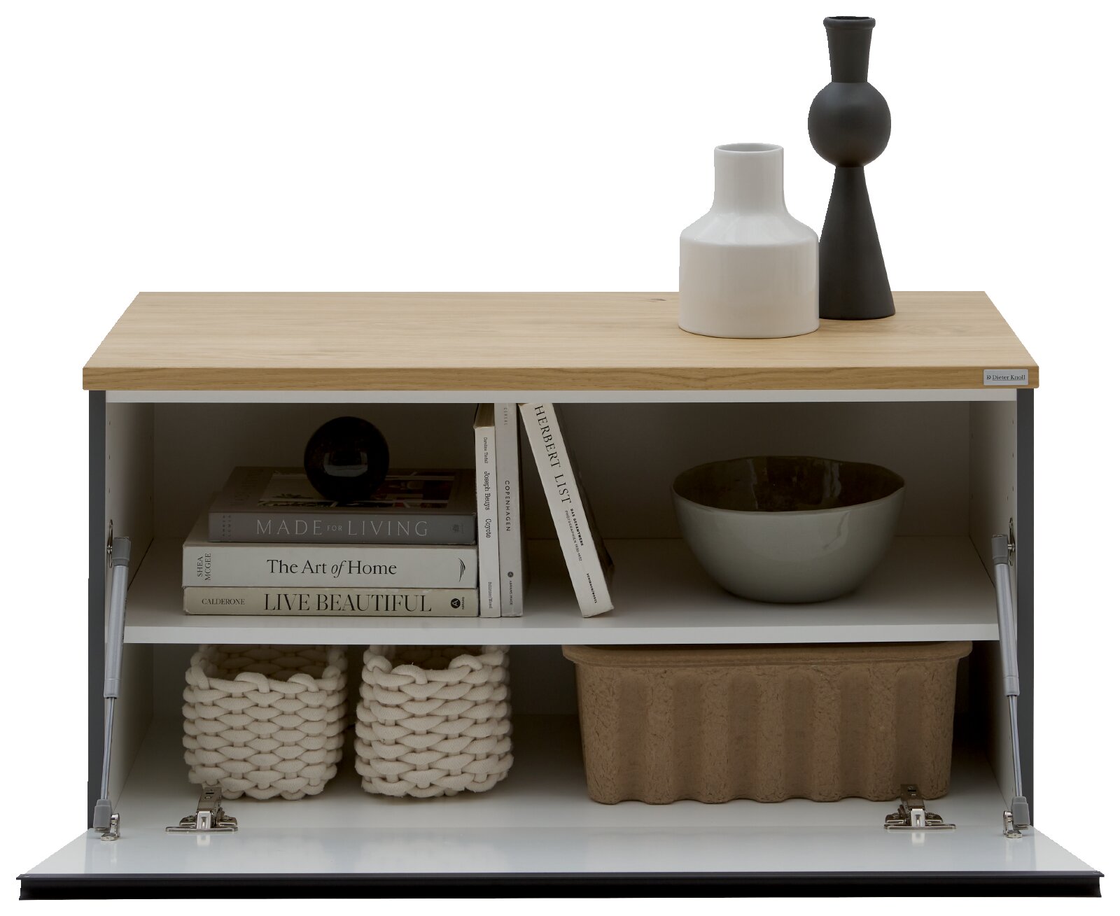 Dieter Knoll Lowboard LENDINA Frontansicht eines modernen Sideboards mit geöffneter Klappe, Holzplatte und grauem Korpus; oben zwei Vasen in Schwarz und Weiß, innen Bücher, Schale und Aufbewahrungskörbe