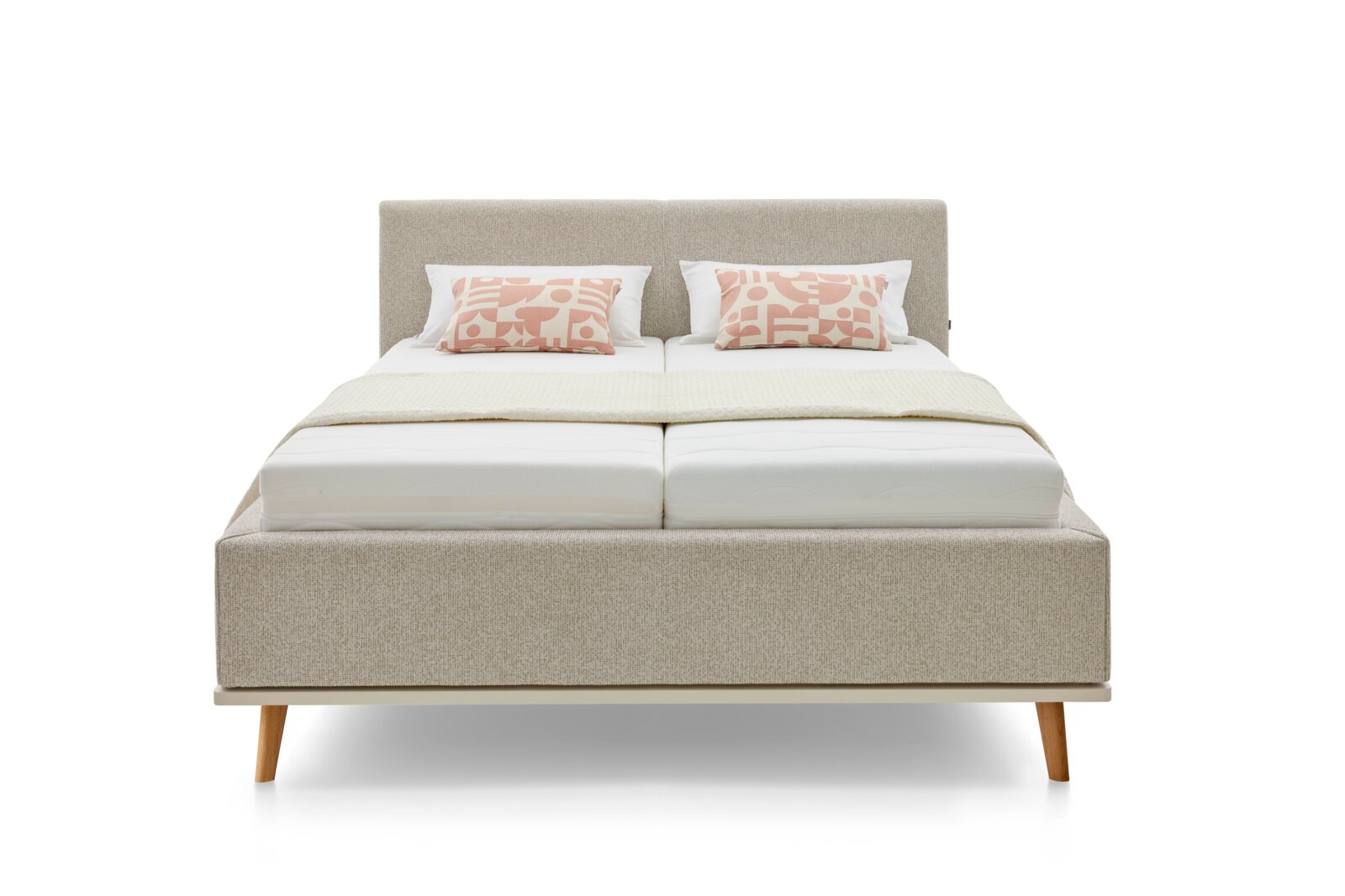 Vooraanzicht van een modern gestoffeerd bed met een beige stoffen bekleding, twee sierkussens en houten poten.