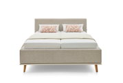 Vooraanzicht van een modern gestoffeerd bed met een beige stoffen bekleding, twee sierkussens en houten poten.