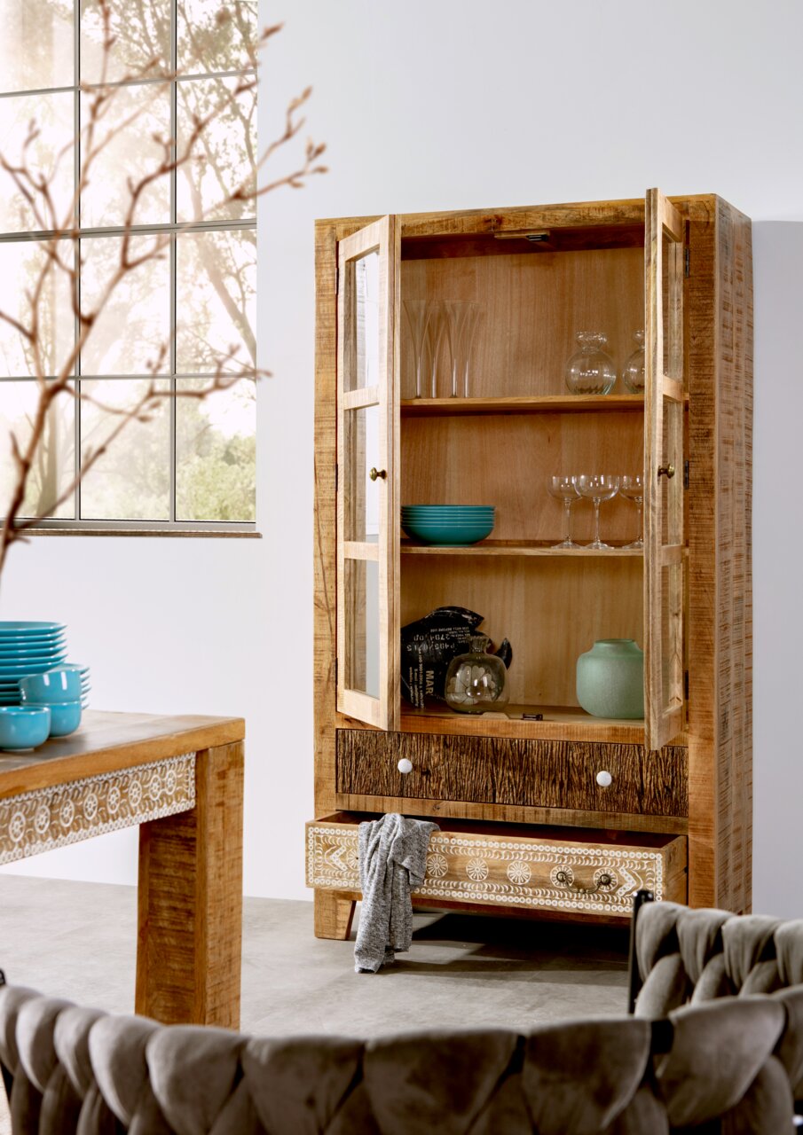 Holzvitrine mit Glastüren, dekoriert mit Geschirr und Gläsern, in einem modernen Wohnzimmer mit Blick auf ein großes Fenster.