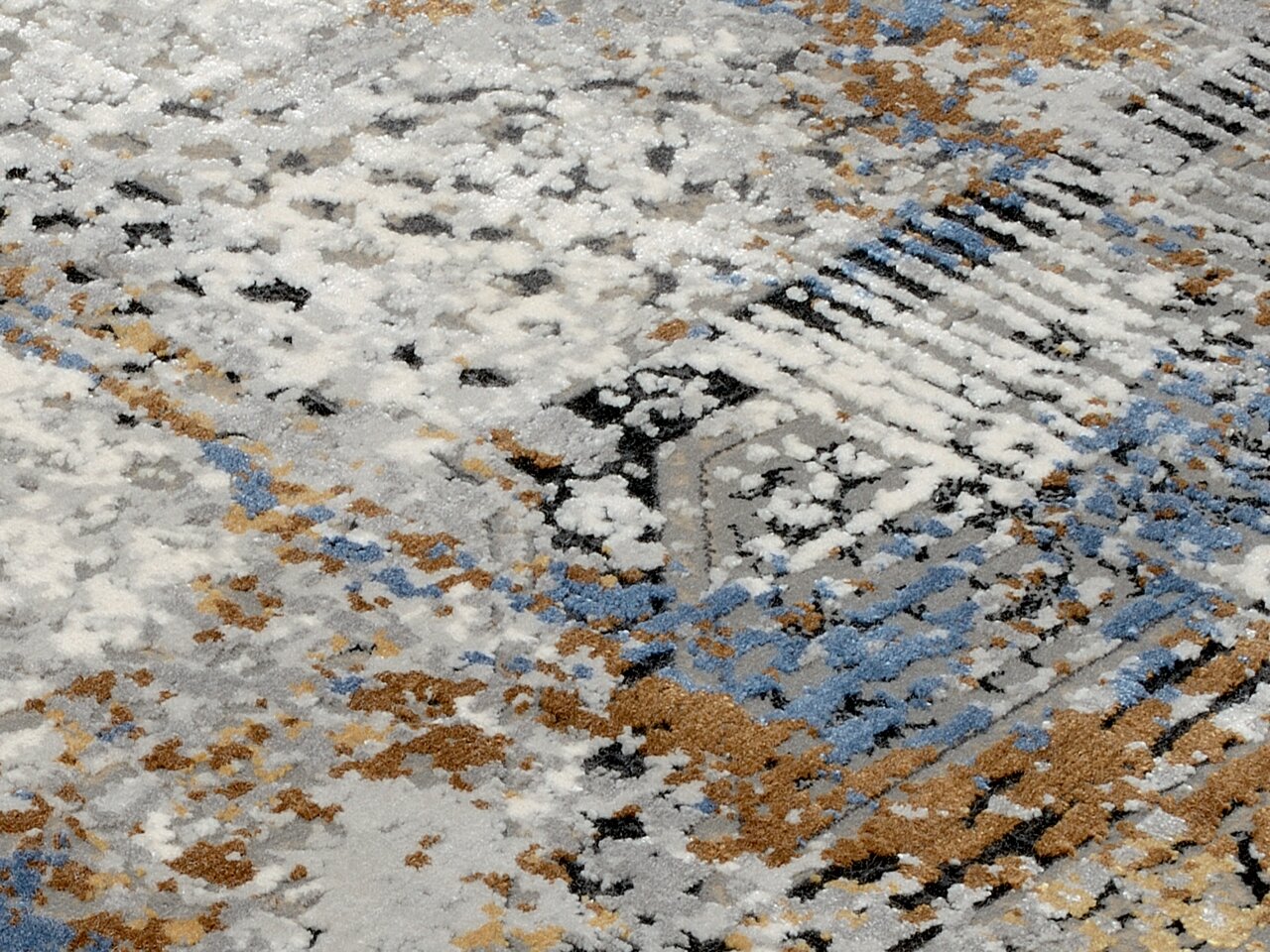 Nahaufnahme eines Designer-Teppichs mit abstraktem Muster in Blau-, Grau- und Brauntönen, von schräg oben fotografiert.