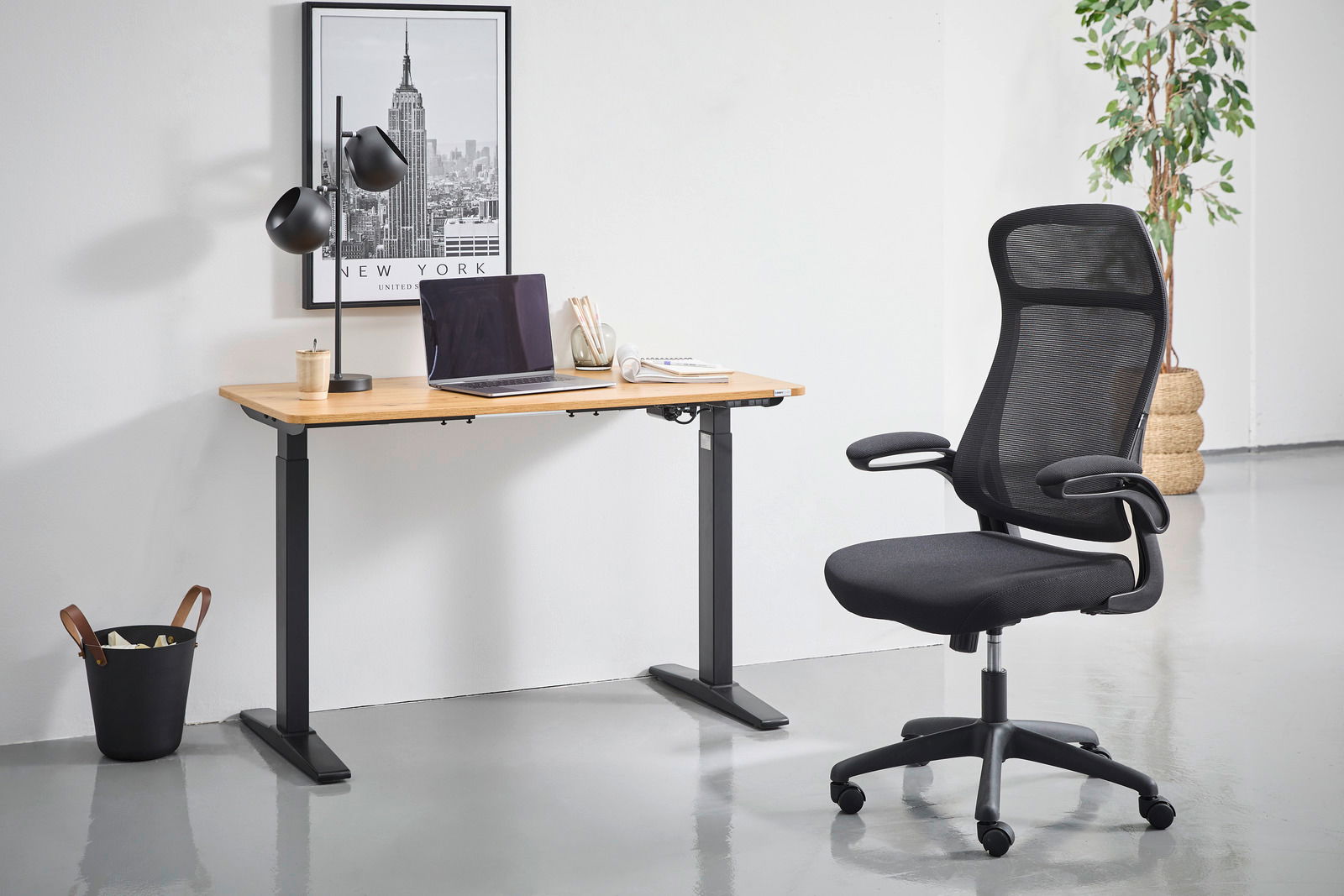 Moderner schwarzer Drehstuhl mit Netzrückenlehne und Armlehnen, seitliche Perspektive, neben einem höhenverstellbaren Schreibtisch in einem minimalistischen Büro.