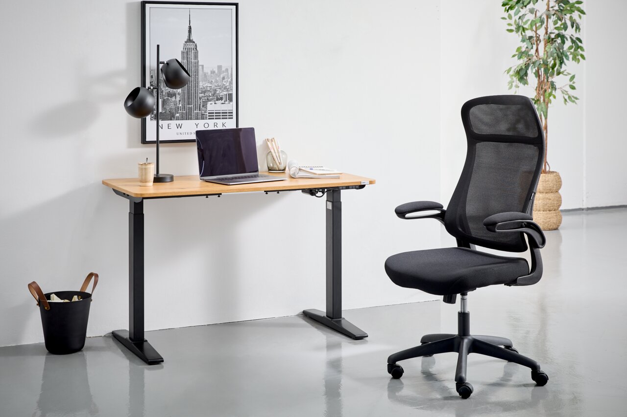 Moderner schwarzer Drehstuhl mit Netzrückenlehne und Armlehnen, seitliche Perspektive, neben einem höhenverstellbaren Schreibtisch in einem minimalistischen Büro.