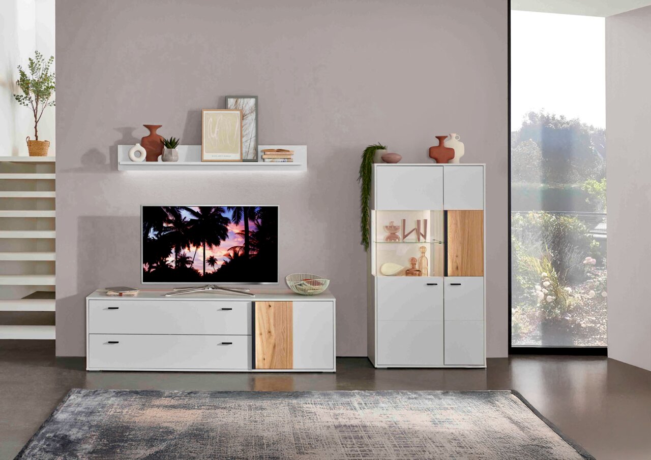 Wohnzimmeransicht mit modernem TV-Lowboard, Wandboard und Highboard in Weiß mit Holzakzenten, dekoriert mit Vasen und Pflanzen, seitliche Perspektive.