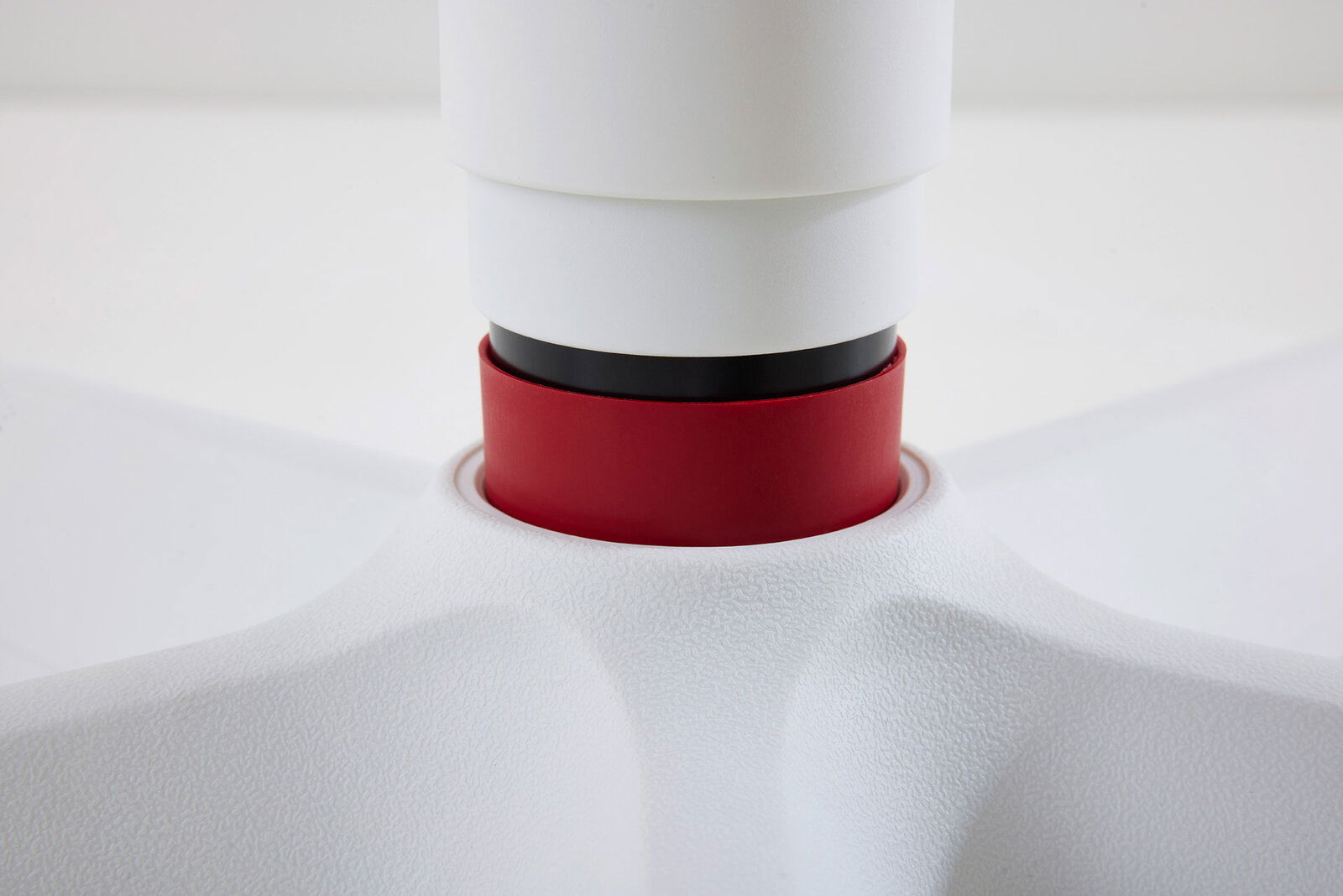 Nahaufnahme eines Jugenddrehstuhls mit weißer und roter Farbgebung, Fokus auf die Verbindung zwischen Sitz und Basis.