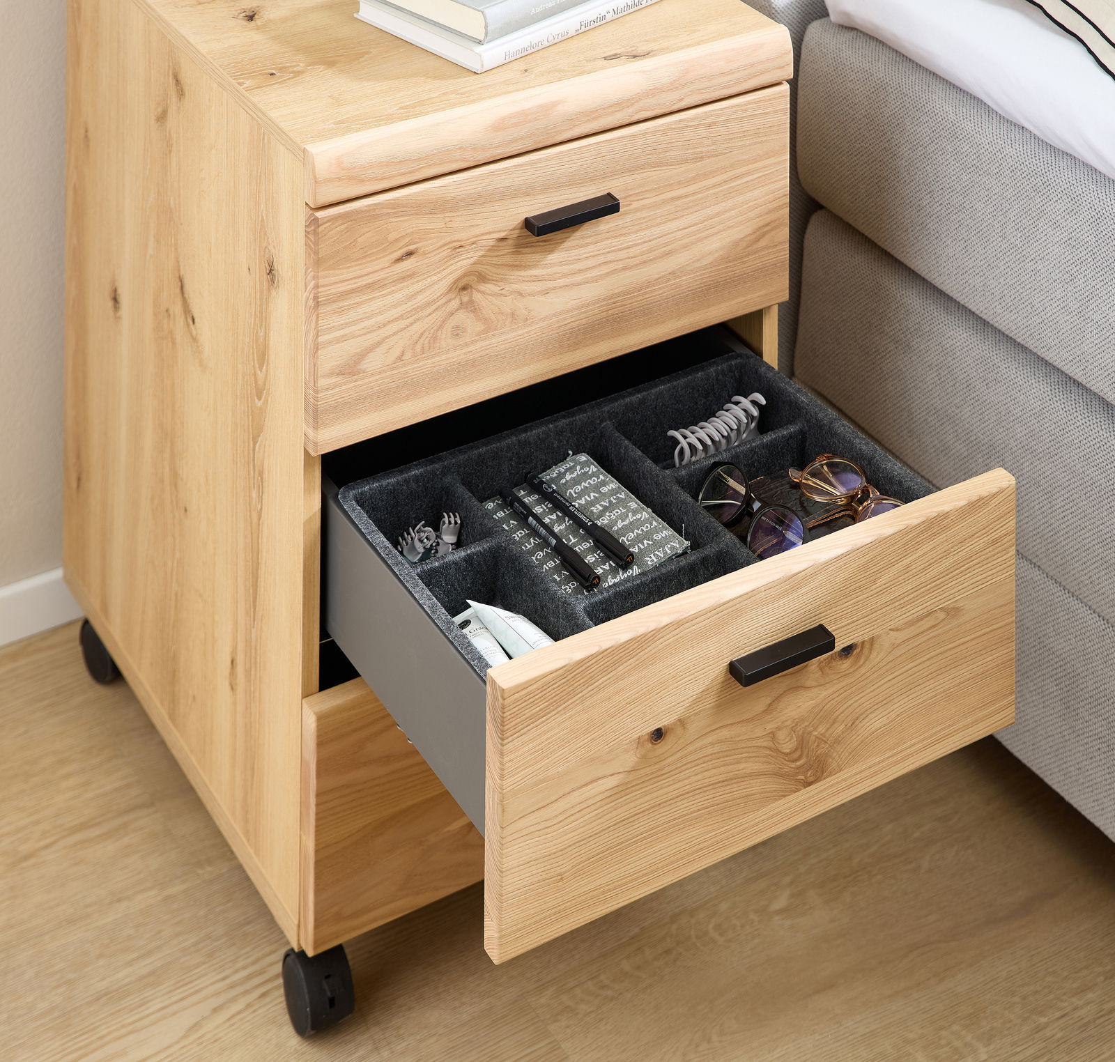 Rollcontainer aus Holz mit zwei Schubladen, eine davon geöffnet und mit Fächern für Accessoires, seitliche Perspektive