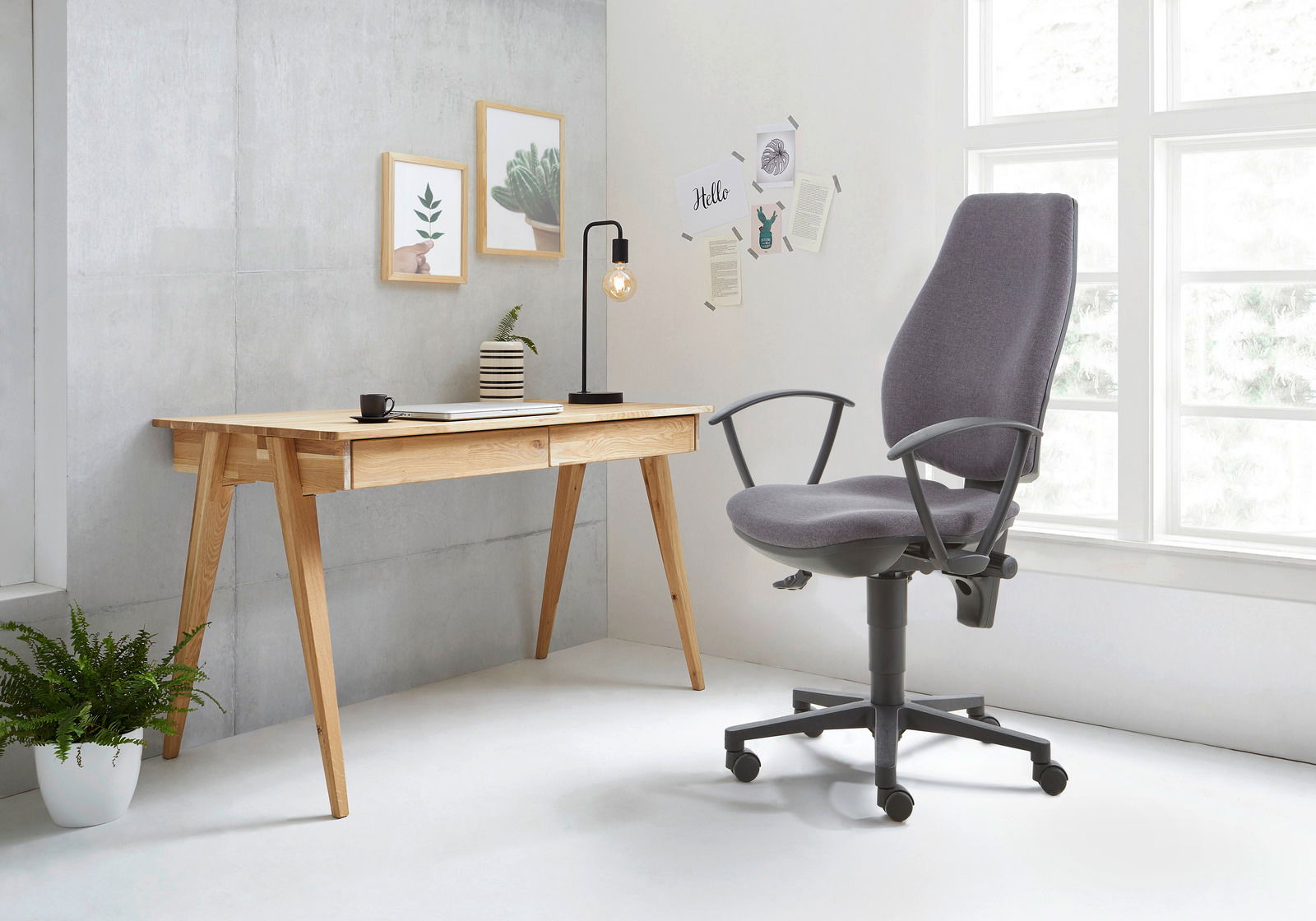 Moderner Schreibtisch aus Holz mit zwei Schubladen, seitliche Perspektive, neben einem ergonomischen Bürostuhl in einem hellen Raum mit großen Fenstern.