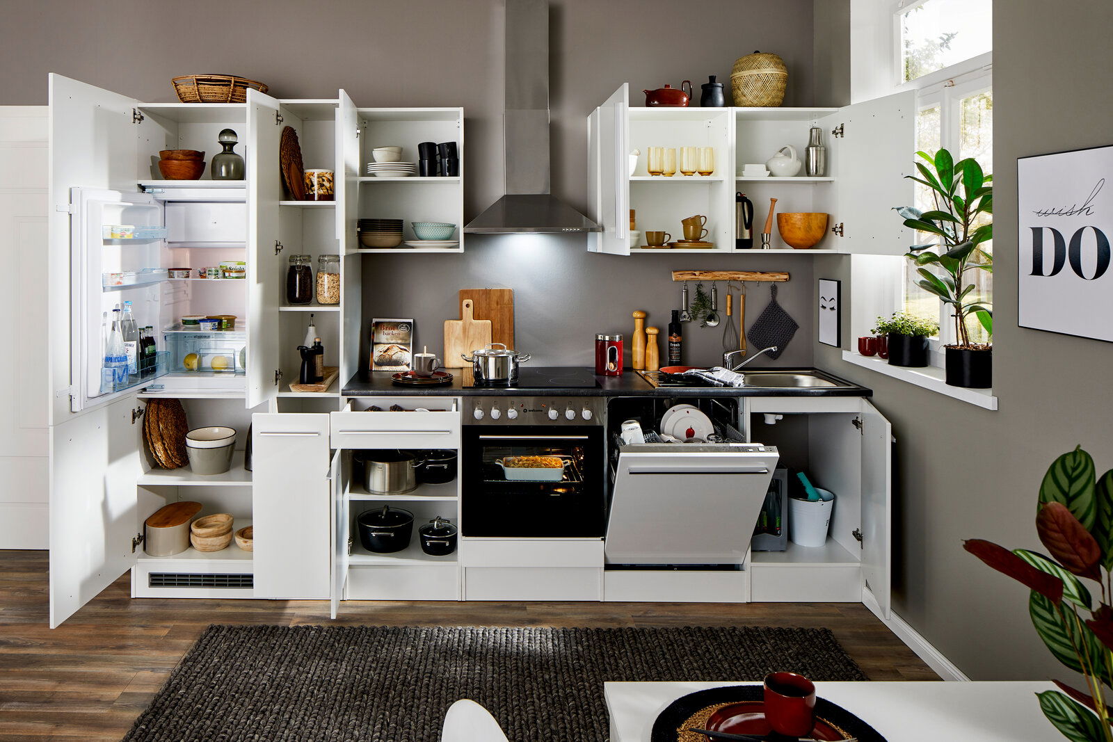 Moderne Küchenzeile in Weiß mit offenen Schränken, Kühlschrank, Herd und Spülmaschine, aus der Frontperspektive fotografiert.