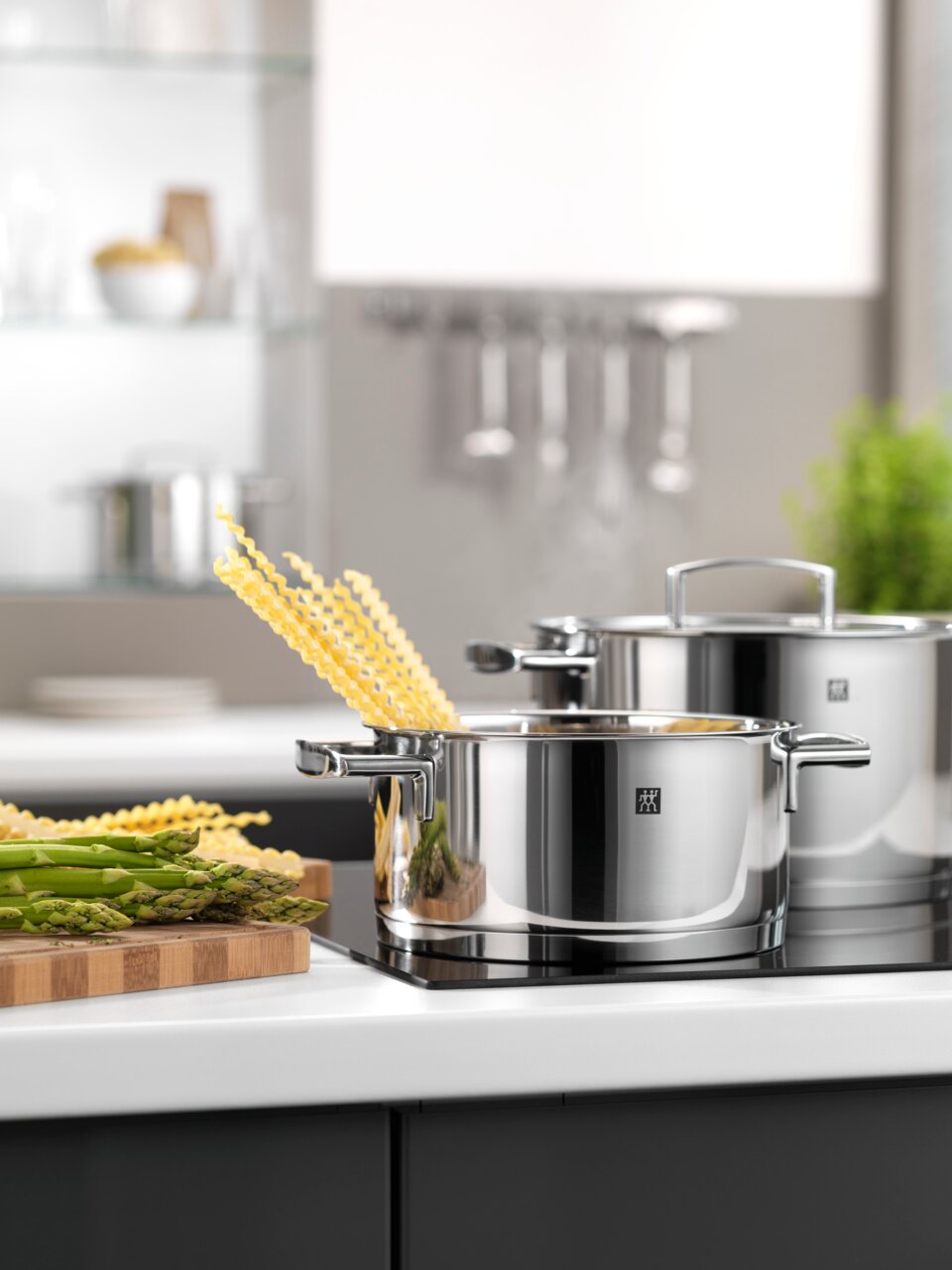 Topfset 5-teilig Passion aus Edelstahl, in moderner Küche auf Herdplatte, mit Spargel und Pasta, seitliche Perspektive