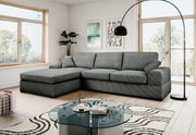 Modernes graues Ecksofa mit linksseitiger Ottomane und drei Sitzkissen in hellem Wohnzimmer, Frontansicht leicht schräg von vorn.