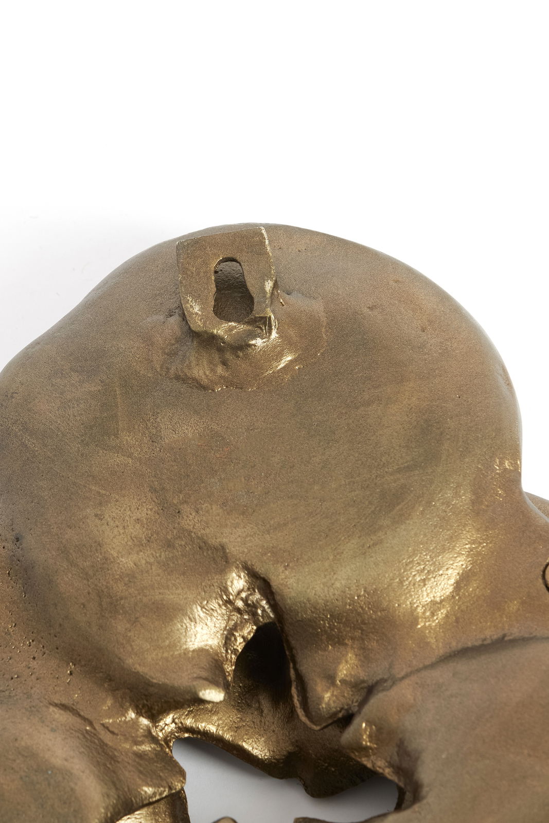 Nahaufnahme eines goldfarbenen Wandornaments mit einer Aufhängung auf der Rückseite, perspektivisch von oben fotografiert.