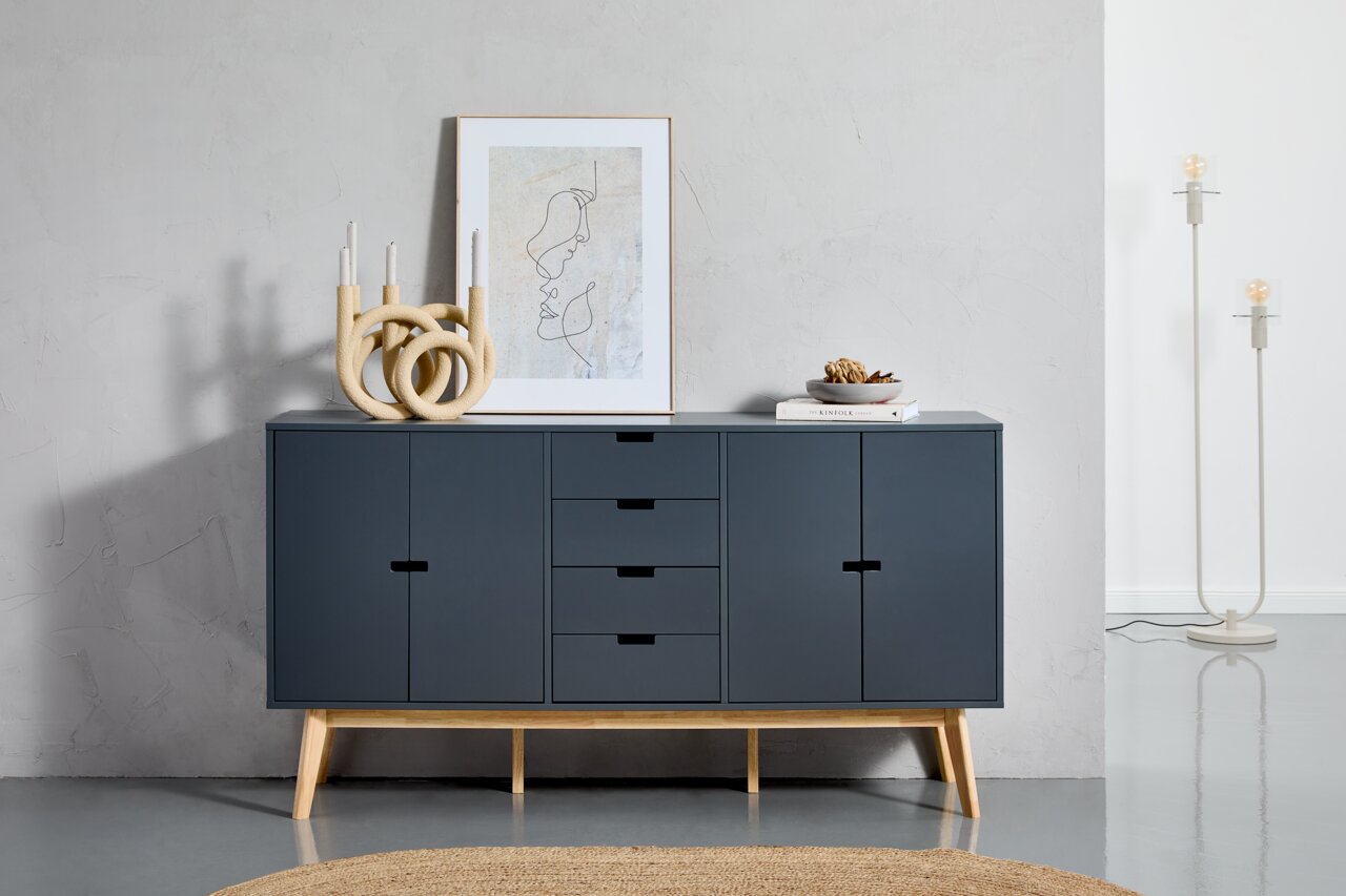 Modernes Sideboard in dunklem Blau mit Holzbeinen, frontal fotografiert. Dekoriert mit einer abstrakten Skulptur, einem gerahmten Kunstwerk und einer Schale auf Büchern.