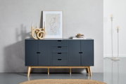 Modernes Sideboard in dunklem Blau mit Holzbeinen, frontal fotografiert. Dekoriert mit einer abstrakten Skulptur, einem gerahmten Kunstwerk und einer Schale auf Büchern.