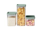 Dreiteiliges Vorratsdosen-Set mit grünen Deckeln, gefüllt mit Reis, Nudeln und Süßigkeiten, aus frontaler Perspektive.
