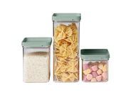 Dreiteiliges Vorratsdosen-Set mit grünen Deckeln, gefüllt mit Reis, Nudeln und Süßigkeiten, aus frontaler Perspektive.