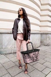 Frau in eleganter Kleidung hält einen stilvollen, rosa gemusterten Einkaufskorb in der Hand, seitliche Perspektive.