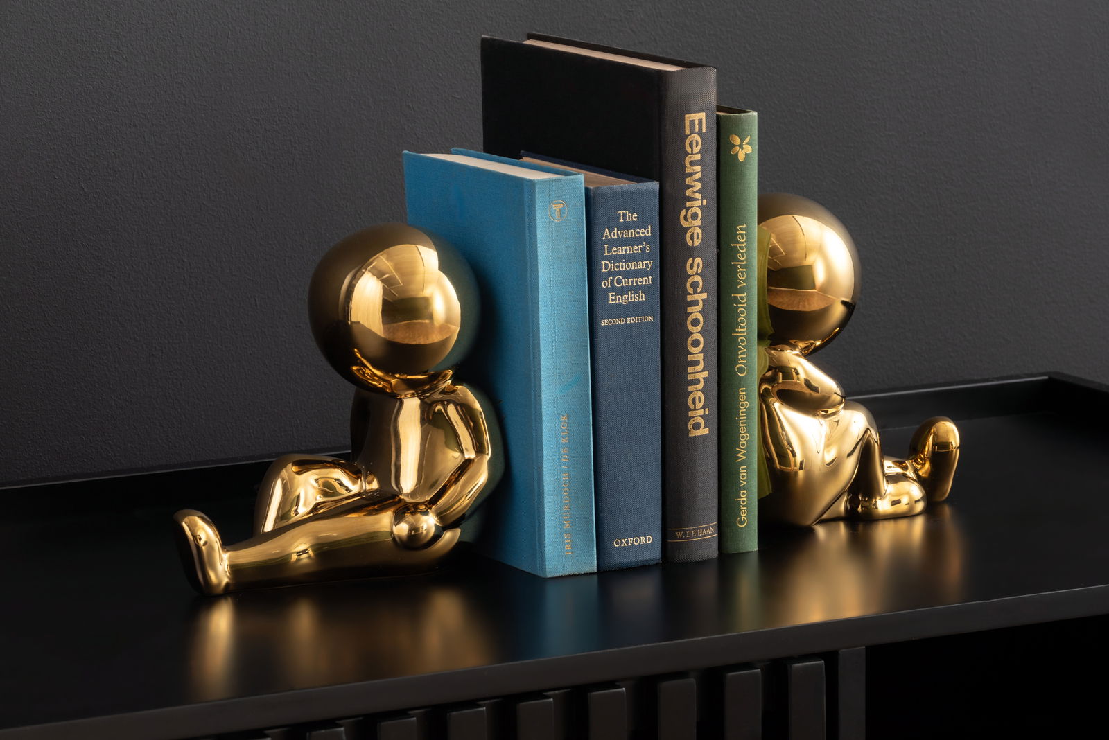 Zwei goldene Buchstützen in Form von sitzenden Figuren, die Bücher auf einem Regal halten, seitliche Perspektive.