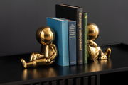 Zwei goldene Buchstützen in Form von sitzenden Figuren, die Bücher auf einem Regal halten, seitliche Perspektive.
