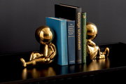 Zwei goldene Buchstützen in Form von sitzenden Figuren, die Bücher auf einem Regal halten, seitliche Perspektive.