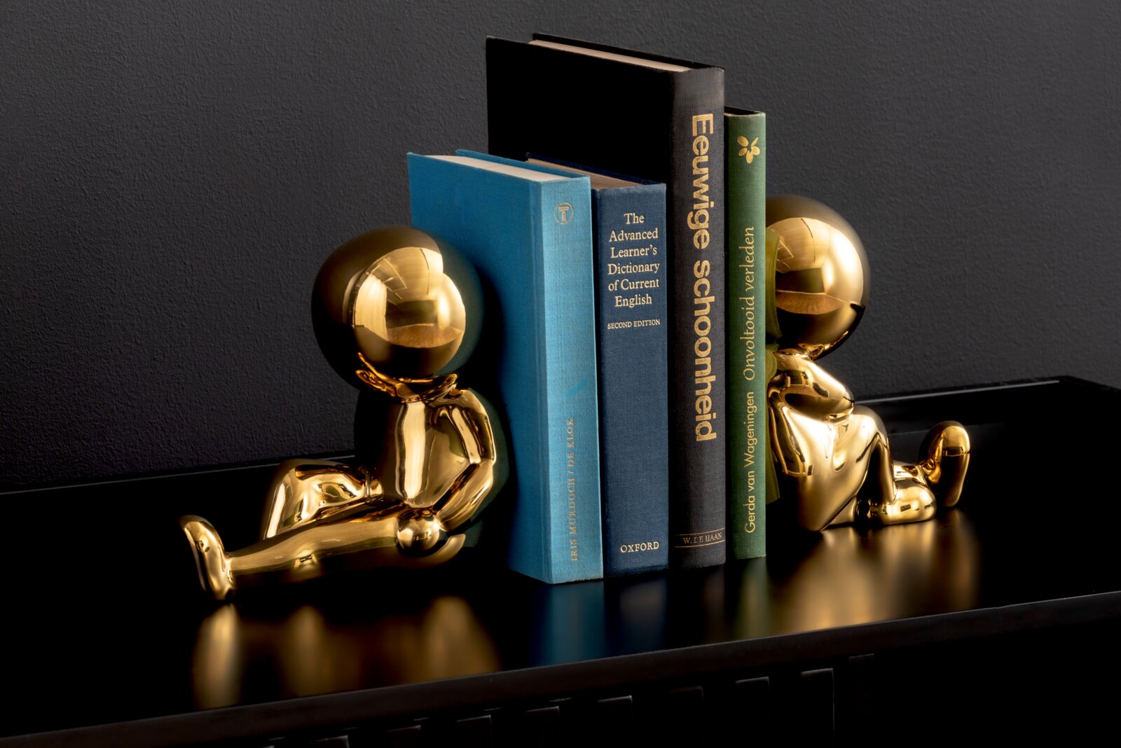present time Buchhalter 2-tlg. JOEY Zwei goldene Buchstützen in Form von sitzenden Figuren, die Bücher auf einem Regal halten, seitliche Perspektive.