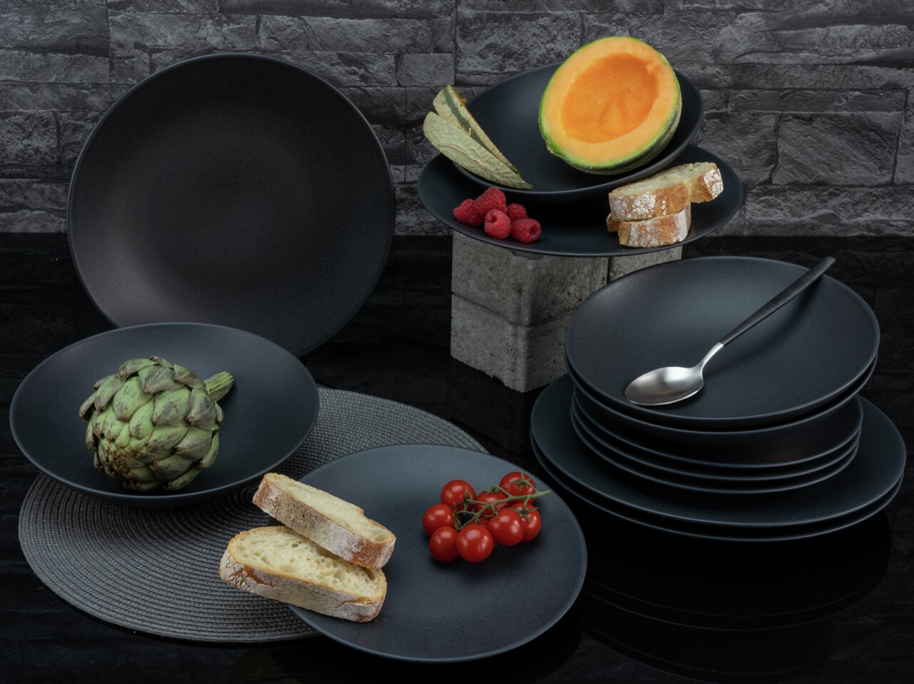 Schwarzes Tafelservice Soft Touch 12-tlg in moderner Steinoptik, präsentiert mit frischem Obst und Gemüse aus einer seitlichen Perspektive.
