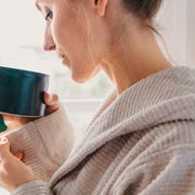 Nahaufnahme einer Person in einem beigen Kapuzenbademantel, die eine Tasse hält.