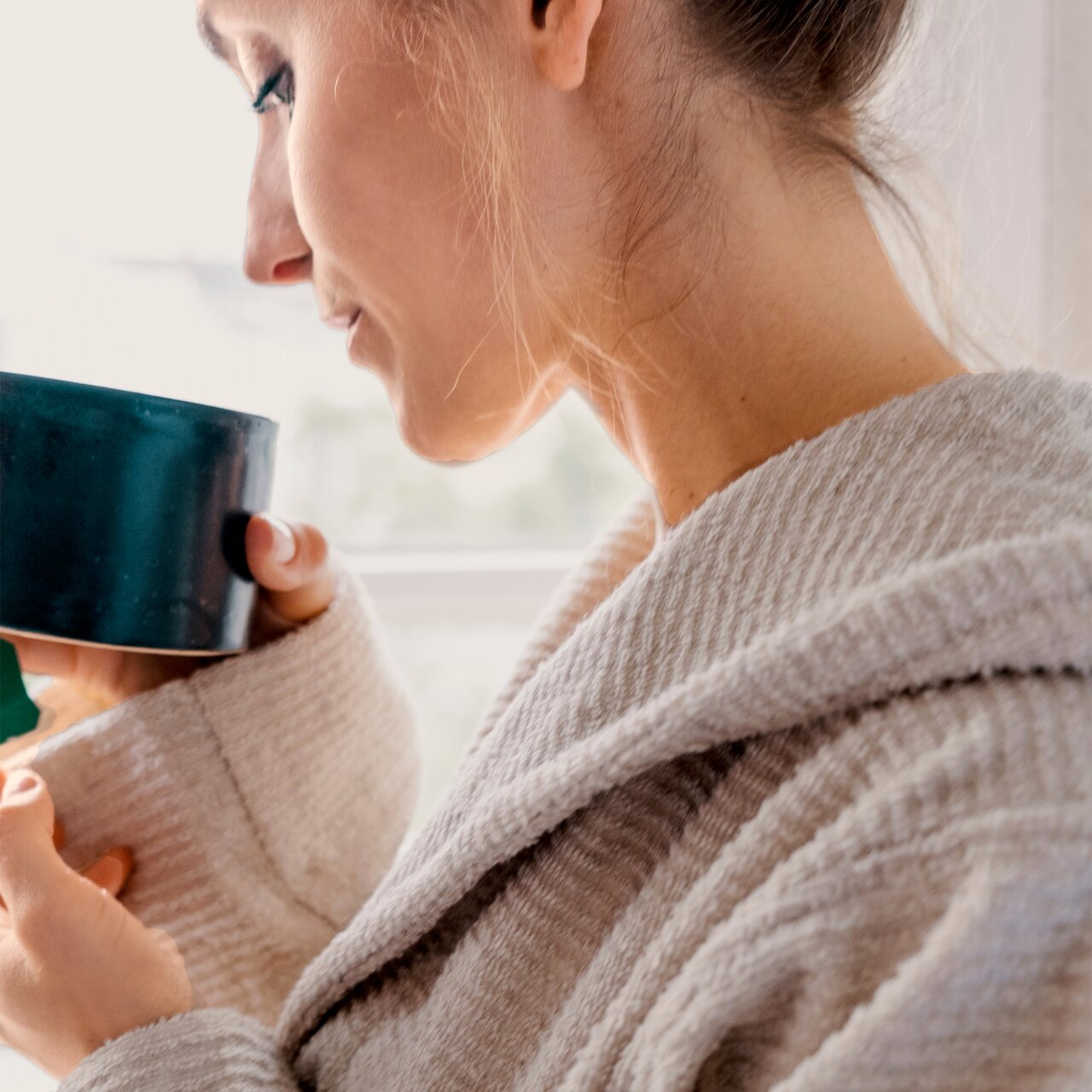 Nahaufnahme einer Person in einem beigen Kapuzenbademantel, die eine Tasse hält.