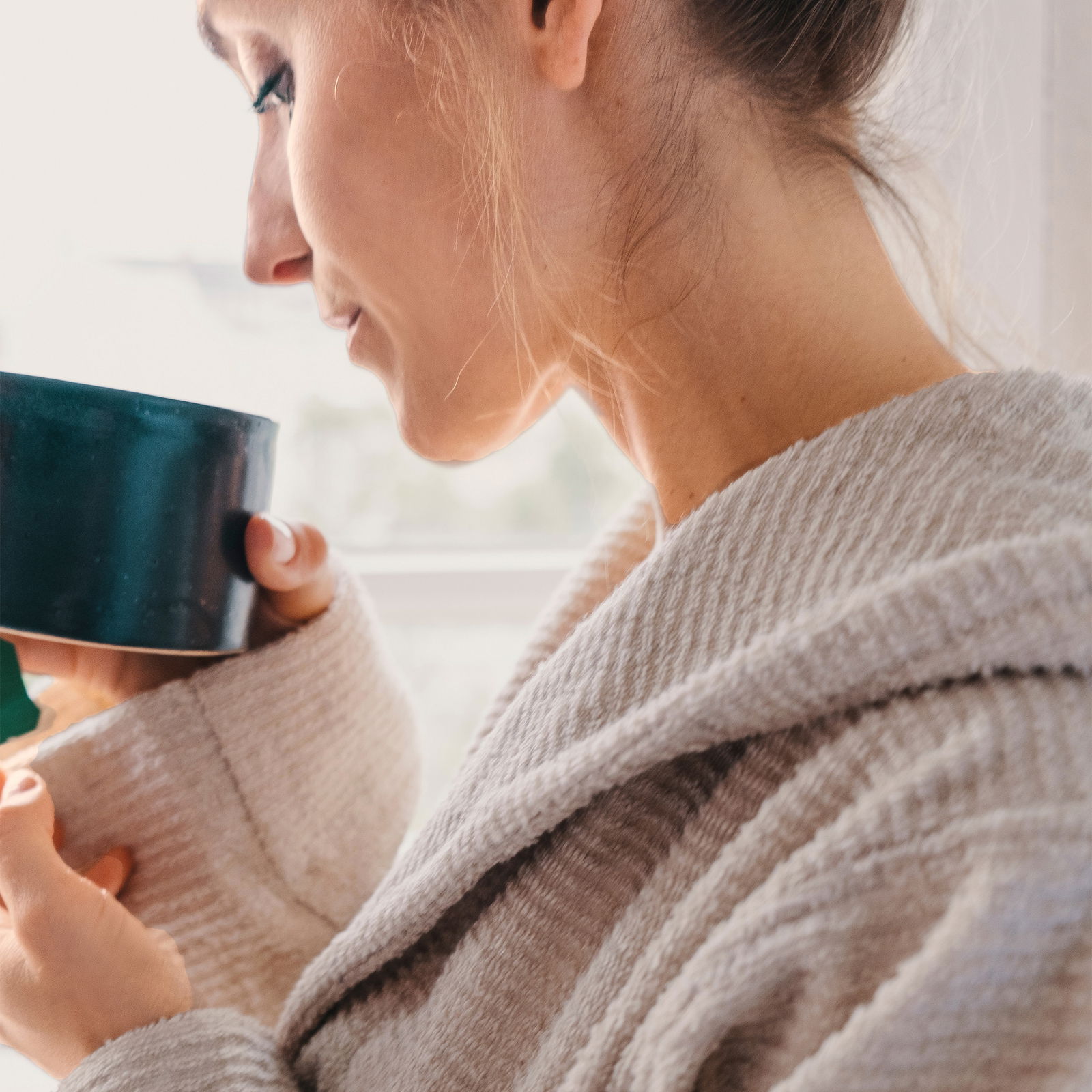 Nahaufnahme einer Person in einem beigen Kapuzenbademantel, die eine Tasse hält.