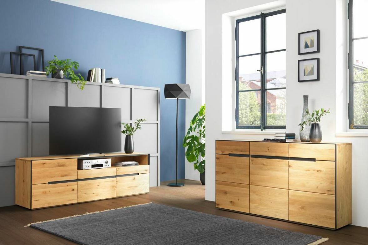 Linea Natura Sideboard KELIO MAX Moderne Wohnzimmermöbel aus Holz, bestehend aus einem TV-Lowboard und einem Sideboard, in einem hellen Raum mit blauen und weißen Wänden, seitliche Perspektive.