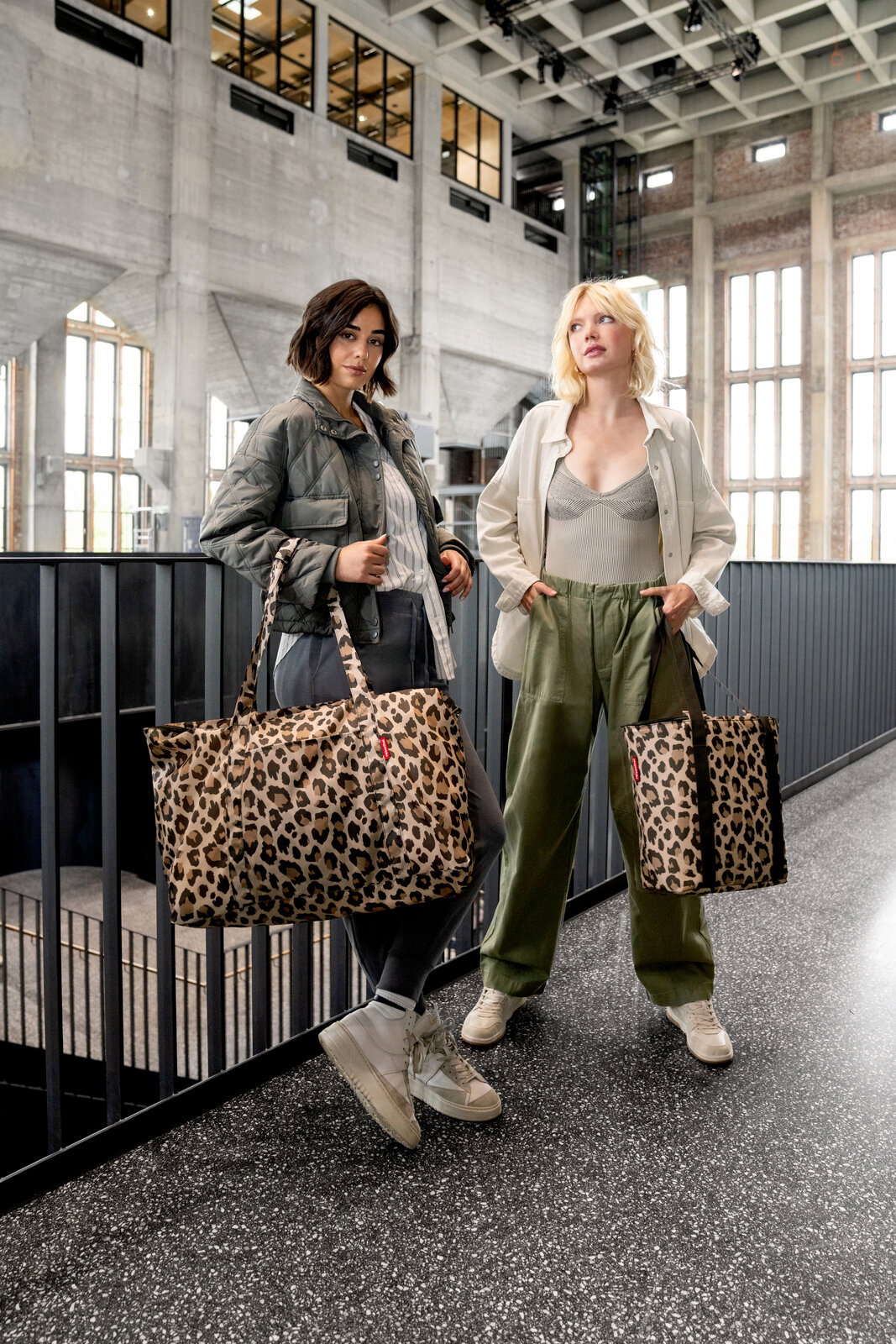 Zwei Frauen stehen in einem modernen Gebäude und halten Leopardenmuster-Kühltaschen in der Hand, fotografiert aus einer frontalen Perspektive.