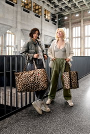 Zwei Frauen stehen in einem modernen Gebäude und halten Leopardenmuster-Kühltaschen in der Hand, fotografiert aus einer frontalen Perspektive.