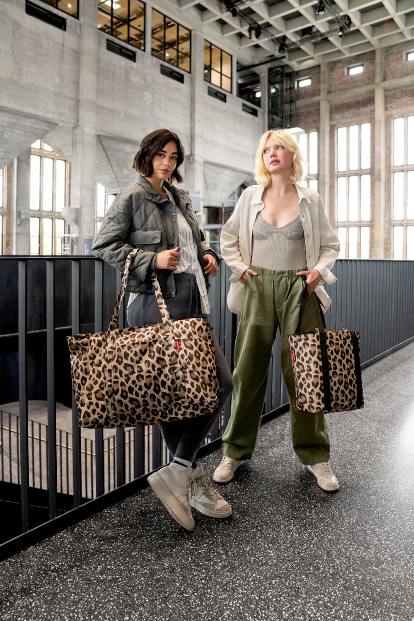 Zwei Frauen stehen in einem modernen Gebäude und halten Leopardenmuster-Kühltaschen in der Hand, fotografiert aus einer frontalen Perspektive.