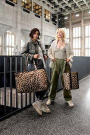 Zwei Frauen stehen in einem modernen Gebäude und halten Leopardenmuster-Kühltaschen in der Hand, fotografiert aus einer frontalen Perspektive.