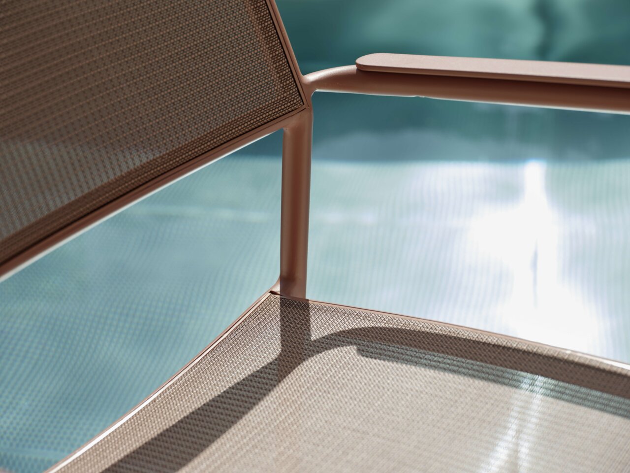 Nahaufnahme eines Stapelsessels mit Metallrahmen und Netzbespannung, im Hintergrund ein verschwommener Pool.