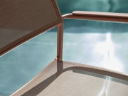 Close-up van een stapelstoel met metalen frame en gaasbekleding, op de achtergrond een wazig zwembad.