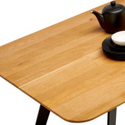 Nahaufnahme eines Esstisches aus Holz mit schwarzem Teeservice und Tellern, Perspektive von oben.