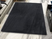 Schwarzer Fellteppich in einem modernen Wohnzimmer, von oben betrachtet, auf hellem Holzboden liegend.