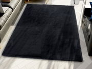 Schwarzer Fellteppich in einem modernen Wohnzimmer, von oben betrachtet, auf hellem Holzboden liegend.