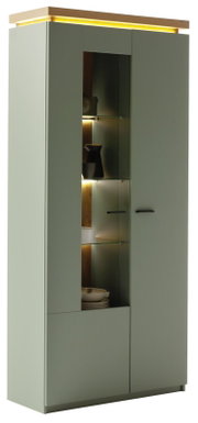 Moderner hoher Vitrinenschrank in mattem Olivgrün mit mittigem Glaseinsatz und LED-Beleuchtung, Holzdeckplatte und schwarzen Griffen, perspektivisch von vorne links fotografiert.