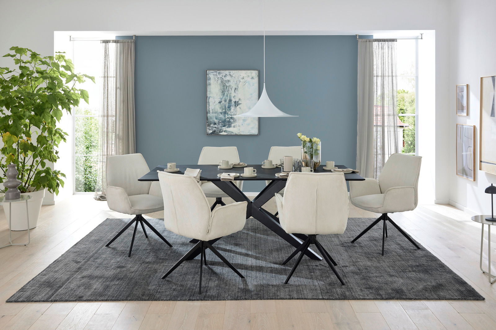 Musterring Esstisch MR TIAMA Esszimmer mit modernem Esstisch und sechs gepolsterten Armlehnstühlen in einem hellen Raum mit großen Fenstern, Blick von vorne.