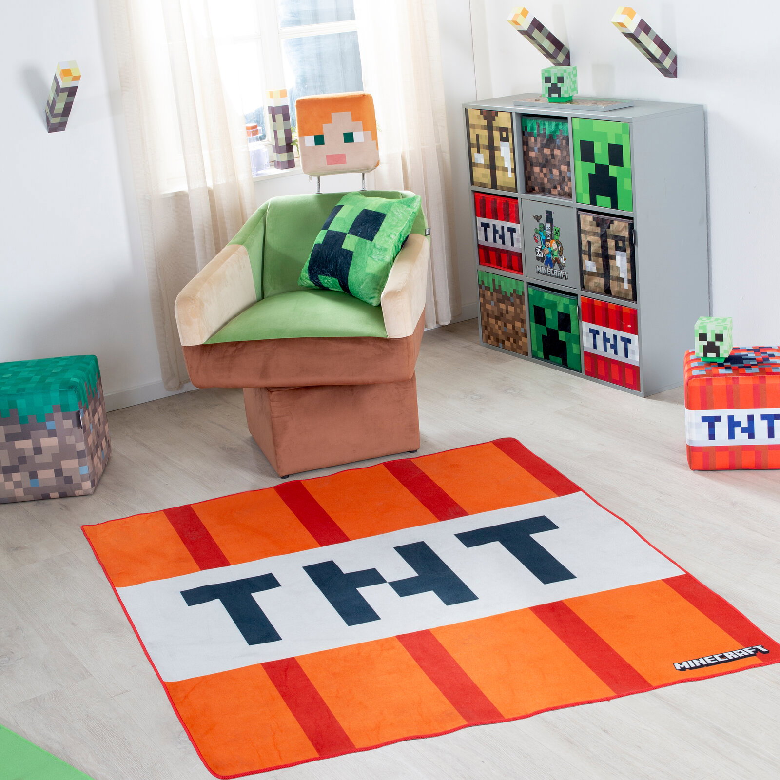 Minecraft TNT-Teppich in Orange und Weiß mit großem „TNT“-Schriftzug, in einem hellen Kinderzimmer auf dem Boden aus schräger Draufsicht (leicht von oben) fotografiert; im Hintergrund Sessel und Minecraft-Deko.