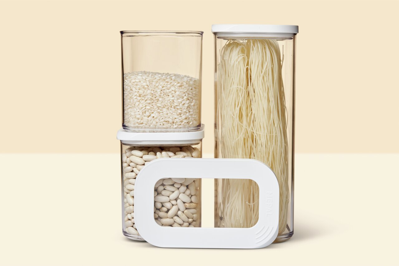 Drei transparente Vorratsbehälter mit weißen Deckeln, gefüllt mit Reis, Bohnen und Nudeln, aus der Frontalperspektive.