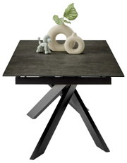 Moderne eettafel met donker tafelblad en sculpturaal onderstel, versierd met stijlvolle accessoires, gezien vanuit het vooraanzicht.
