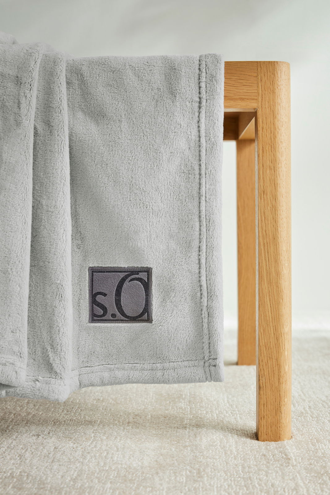 Graue Kuscheldecke von s.Oliver, drapiert über eine Holzkante, Nahaufnahme.