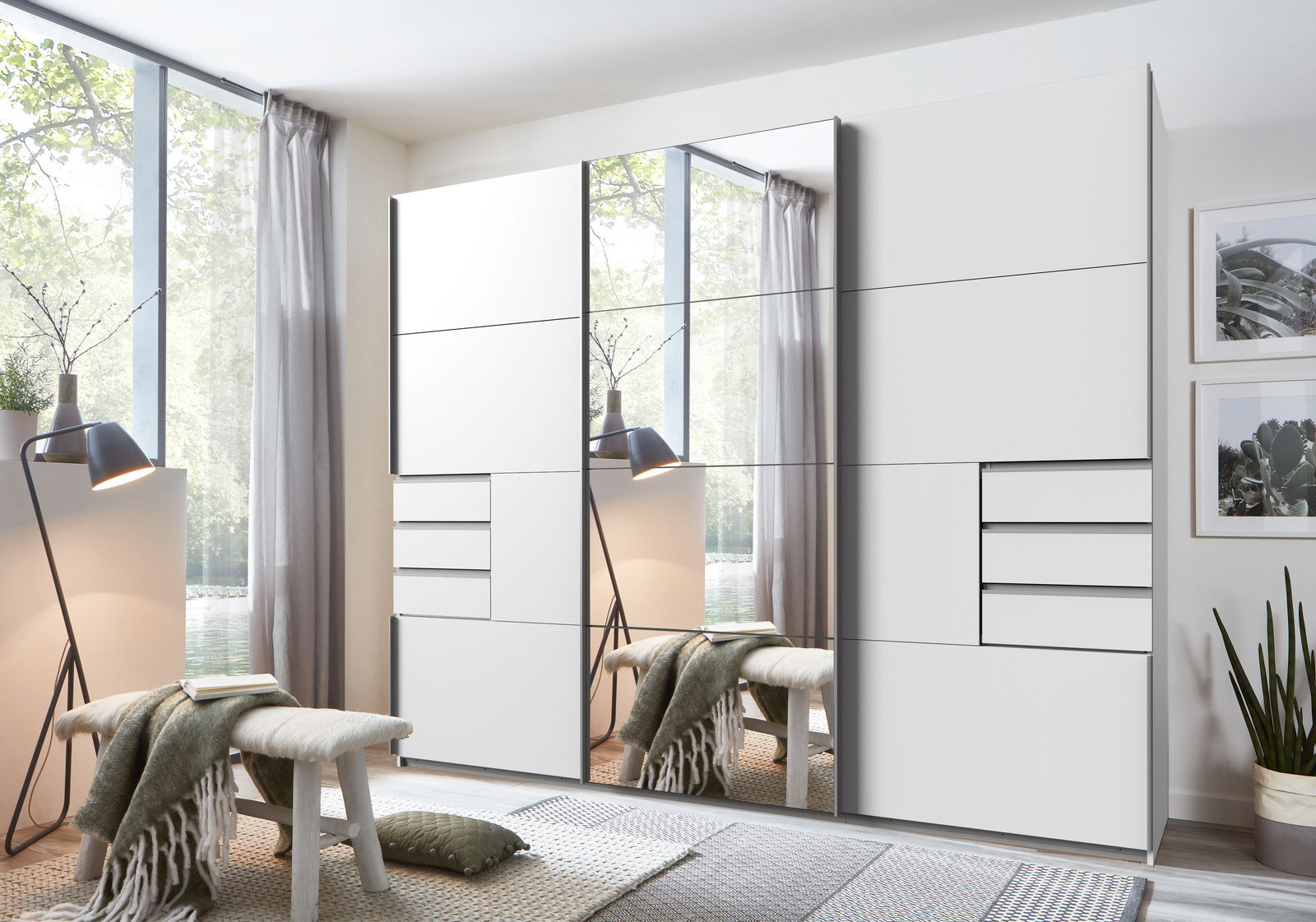 Z2 Hangende kast met 3 deuren SAIGON Moderner Schwebetürenschrank mit drei Türen, teilweise mit Spiegeln, in einem hellen Raum mit Blick auf ein großes Fenster.