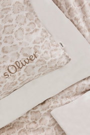 Nahaufnahme einer Satinbettwäsche in Beige mit dezentem Muster und s.Oliver-Logo, von oben fotografiert.