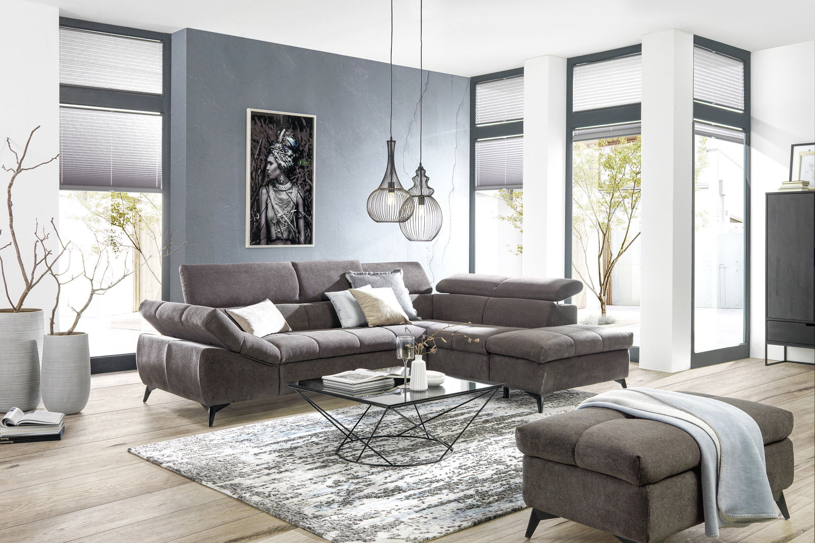 Ecksofa in einem modernen Wohnzimmer mit grauem Stoffbezug, dekoriert mit Kissen, im Vordergrund ein Couchtisch und ein Hocker, seitliche Perspektive.