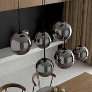 Schwarze Pendelleuchte mit mehreren spiegelnden Kugel-Schirmen aus Metall, hängend über einem Esstisch in modernem Interieur, schräg von oben aus der Seitenansicht aufgenommen