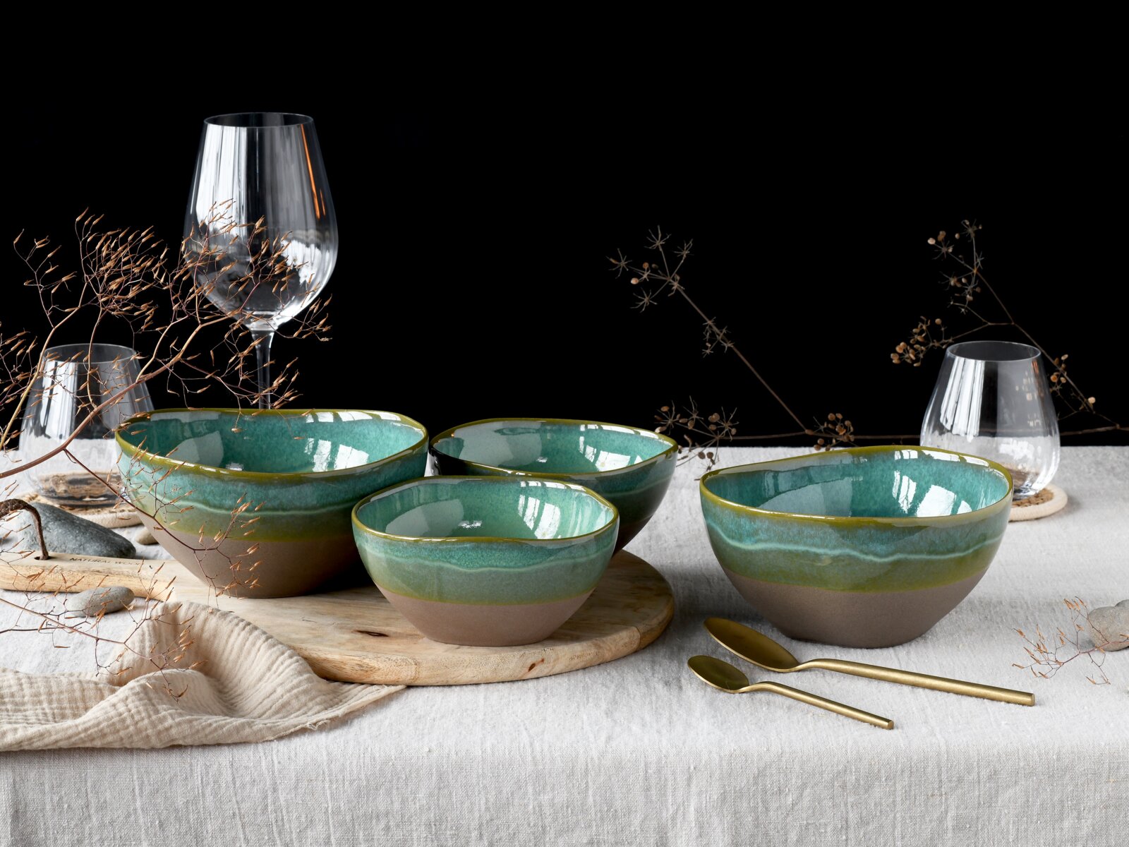 Creatable Bowl 4-tlg BASALT BIO Schüssel-Set aus Keramik in Grün-Türkis mit braunem Fuß, auf einem gedeckten Tisch arrangiert; Perspektive: frontale Ansicht auf Tischhöhe.