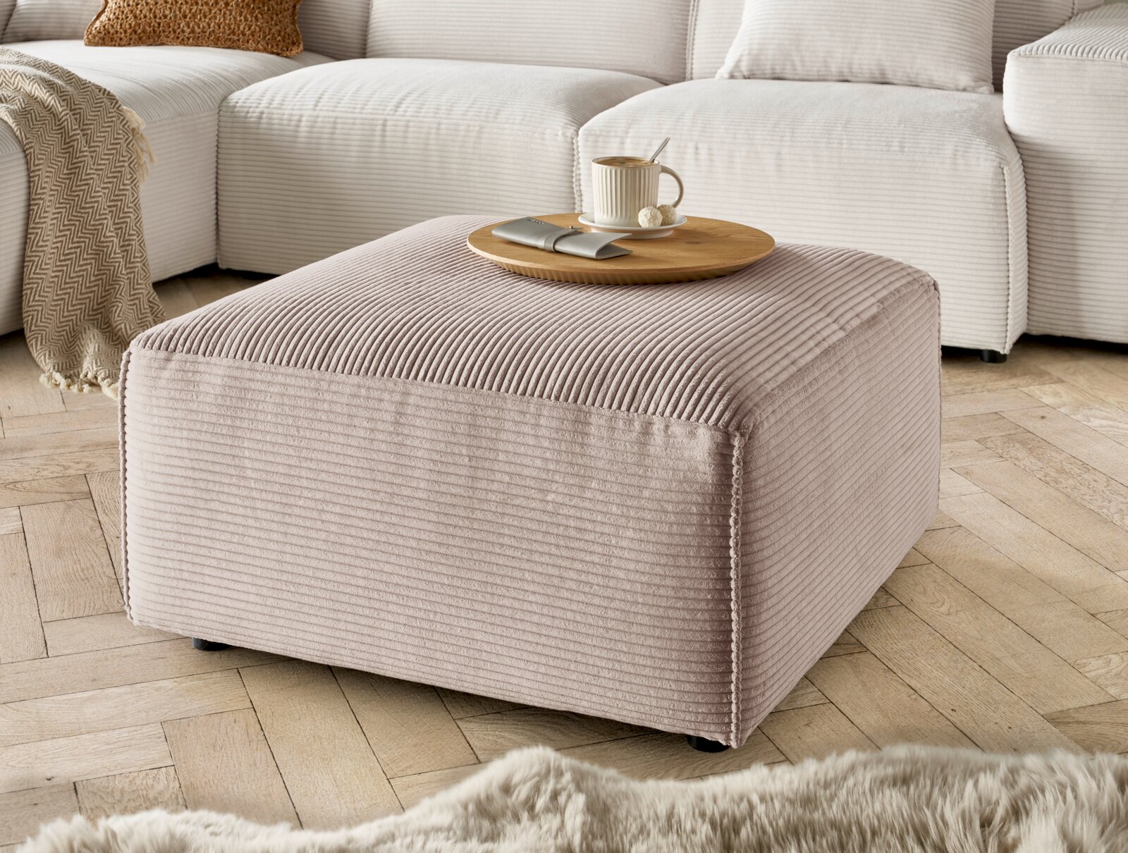 Lounge Handmade Hocker LH-EDINA Hocker in Nahaufnahme, beige gestreifter Stoff, mit Tablett und Tasse darauf, auf Holzfußboden vor einem Sofa.